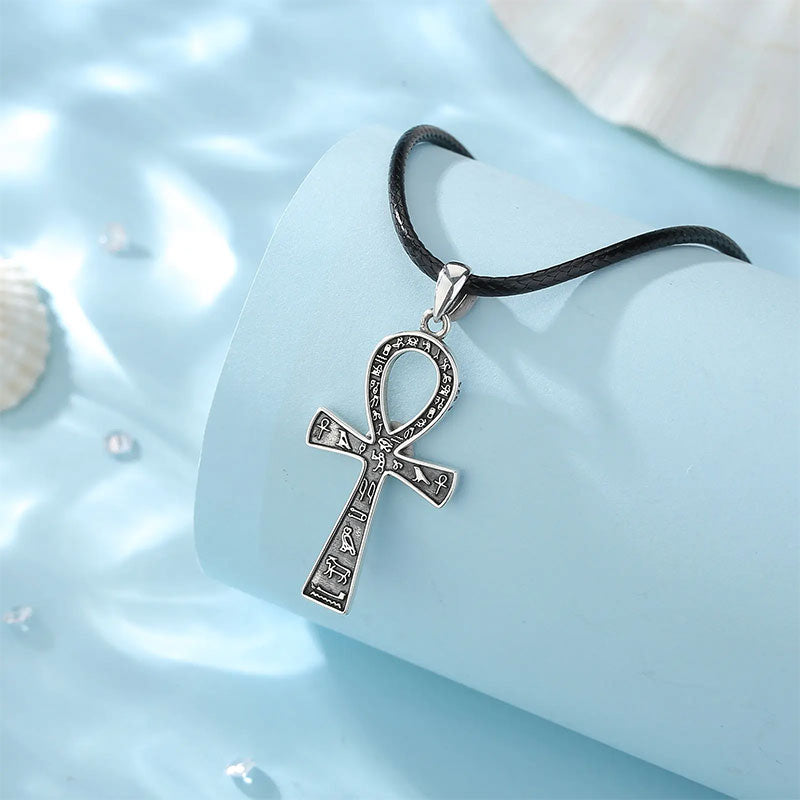 Colar Prata Masculino Ankh em prata 925, com cordão preto, fotografado sobre fundo azul com conchas e reflexos d’água.