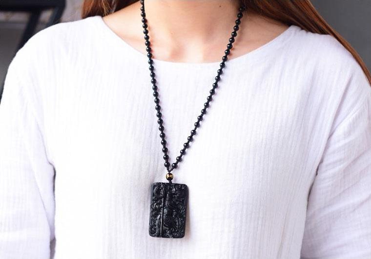 Pessoa usando o Colar Obsidiana Guan Yu, o colar se destaca sobre blusa branca.